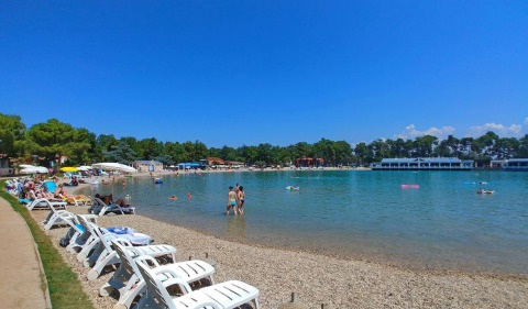 Zonnige ligstoelen en zwemmers bij Camping Stella Maris vakantiepark in Istrië, Kroatië, onder een blauwe lucht.