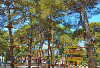 Parc d'aventure au Camping Stella Maris en Istrie, Croatie, avec des gens grimpant et marchant dans les arbres.
