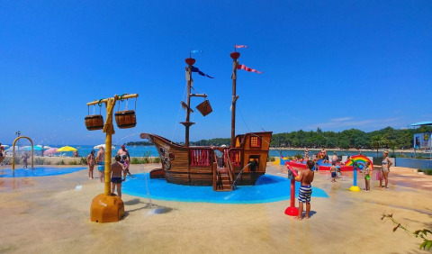 Bambini giocano in un'area giochi acquatica con nave dei pirati al Camping Stella Maris in Istria, Croazia, sotto il sole.