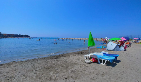 Beach with umbrellas, sunbeds, and people swimming near Umag, Istria, Croatia on a sunny day.