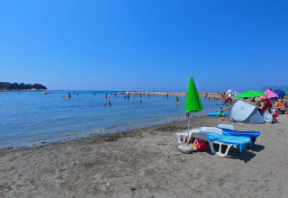 Spiaggia con ombrelloni, lettini e bagnanti vicino a Umag, Istria, Croazia, in una giornata soleggiata.