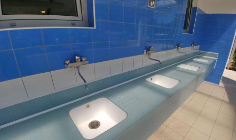 Fila de lavabos modernos bajo azulejos azules en Camping Stella Maris, un parque vacacional en Istria, Croacia.