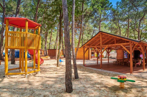 Parque infantil y pabellones de madera en Camping Stella Maris, rodeados de pinos en Istria, Croacia.