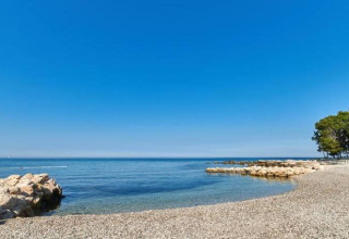 Belle vue sur la plage de galets du Camping Stella Maris en Istrie, Croatie, sous un ciel bleu clair.