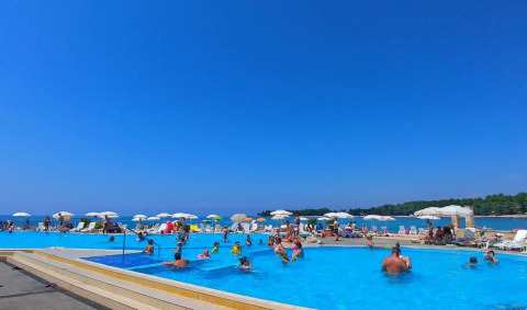 Camping Stella Maris en Istria, Croacia, con huéspedes disfrutando de la piscina y sombrillas junto al mar.