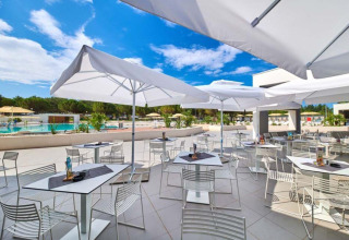 Udendørs caféområde med hvide parasoller og moderne møbler ved poolen i Camping Stella Maris, Istrien, Kroatien.