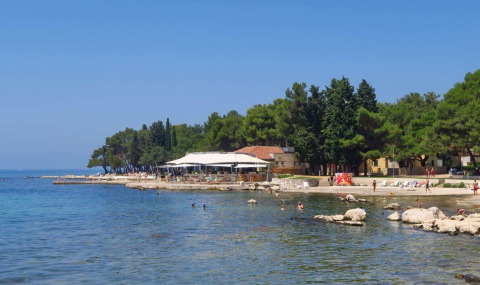 Camping Stella Maris en Istria, Croacia, con bañistas, paseo marítimo y árboles bajo un cielo azul despejado.