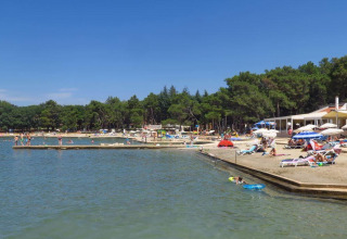 Strandscene nær Umag, Istrien, Kroatien, med badegæster, solsenge og parasoller under blå himmel.