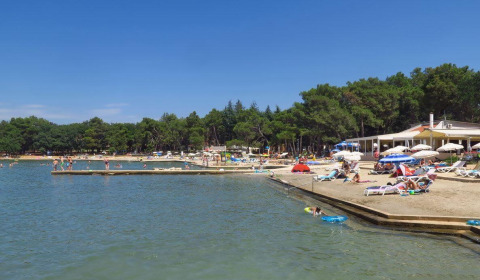 Strand bei Umag in Istrien, Kroatien, mit Menschen, Liegen und Sonnenschirmen an einem sonnigen Tag.