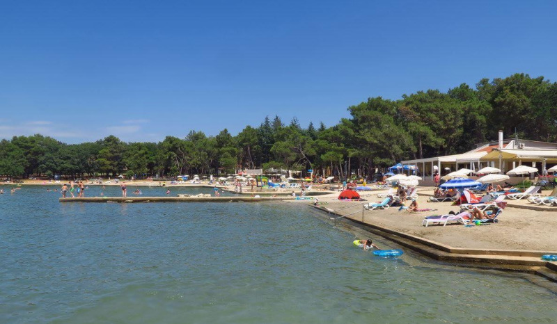 Beach scene near Umag, Istria, Croatia, with sunbathers, umbrellas, and people enjoying a sunny day.