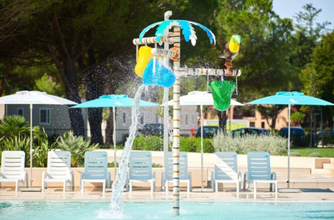 Water play area with colorful buckets and poolside chairs at sunny Camping Stella Maris, Istria, Croatia.
