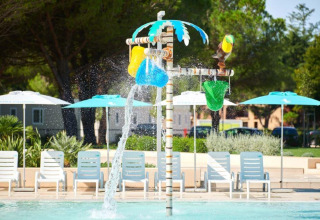 Water play area with colorful buckets and poolside chairs at sunny Camping Stella Maris, Istria, Croatia.