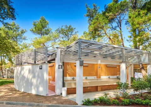 Moderne Sanitäranlagen im Camping Stella Maris, Istrien, Kroatien, umgeben von Bäumen und strahlendem Himmel.