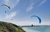 Vier paragliders zweven boven groene heuvels en strand bij Toftum Bjerge Camping in Denemarken.