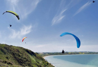 Vier paragliders zweven boven groene heuvels en strand bij Toftum Bjerge Camping in Denemarken.