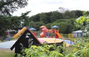 Speeltuin met glijbanen en springkussen in Toftum Bjerge Camping, omringd door bomen en struiken.