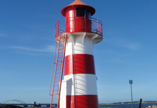 Red and white lighthouse at Toftum Bjerge Camping holiday park in Central Denmark Region, under a clear sky.