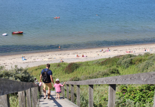 Father and daughter walk down wooden stairs to the sandy beach at Toftum Bjerge Camping, Denmark.