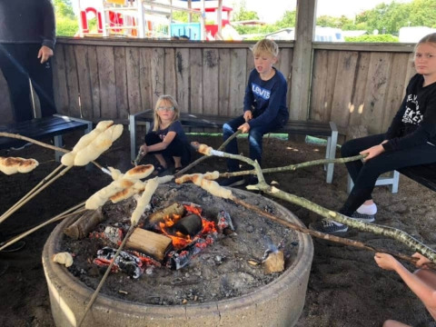 Kinder rösten Brot am Lagerfeuer im Toftum Bjerge Campingplatz in Dänemark unter einer Überdachung.