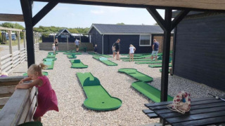 Campo de mini golf en Toftum Bjerge Camping, familias y niños divirtiéndose al aire libre.