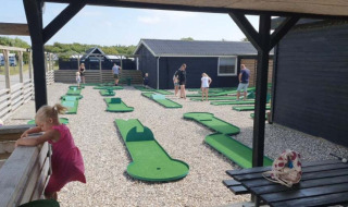 Campo de mini golf en Toftum Bjerge Camping, familias y niños divirtiéndose al aire libre.