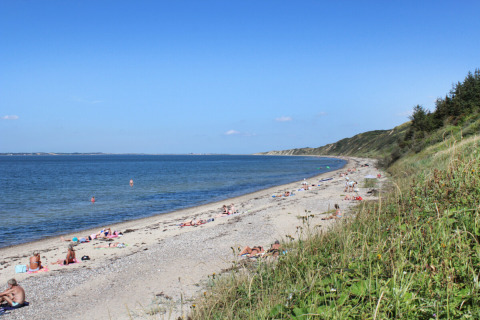 Folk solbader og svømmer på en strand med græsbeklædte klitter nær Struer i Region Midtjylland, Danmark.