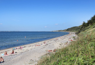Folk solbader og svømmer på en strand med græsbeklædte klitter nær Struer i Region Midtjylland, Danmark.