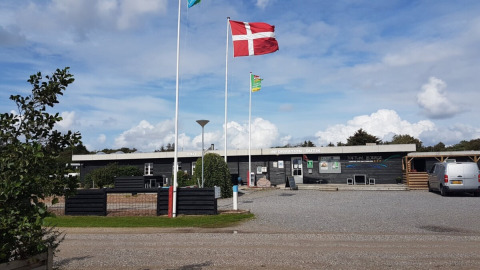 Toftum Bjerge Camping in Denemarken met Deense vlag voor het hoofdgebouw en parkeerplaatsen op de voorgrond.