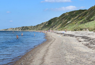Strand ved Toftum Bjerge Camping i Danmark med folk, der bader og klitter dækket af grønt bagved.