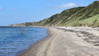 Playa en Toftum Bjerge Camping, Dinamarca, con personas nadando y acantilados verdes al fondo.