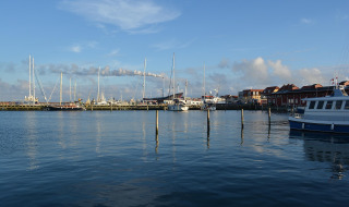 Puerto con barcos y casas cerca del agua en Struer, Dinamarca, bajo un cielo azul con nubes blancas.