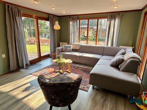 Lys stue i Cozy Lodge, Bungalowpark Het Verscholen Dorp, med stor sofa og udsigt til have i Holland.