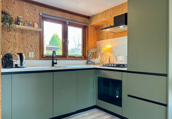 Cucina moderna con mobili verdi, grande finestra e pannelli in legno al Cozy Lodge, Het Verscholen Dorp.