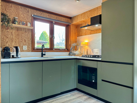 Moderne keuken met groene kasten, groot raam en houtafwerking in Cozy Lodge, Het Verscholen Dorp.