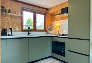 Moderne keuken met groene kasten, groot raam en houtafwerking in Cozy Lodge, Het Verscholen Dorp.