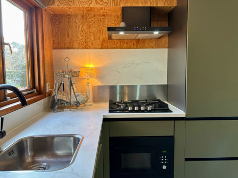 Moderne keukenhoek met gasvuur, gootsteen, microgolfoven en raam in Cozy Lodge in Nederland.