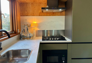 Moderne keukenhoek met gasvuur, gootsteen, microgolfoven en raam in Cozy Lodge in Nederland.