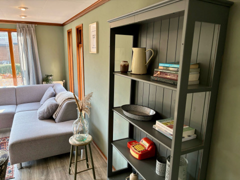 Gezellige woonkamer in Cozy Lodge bij Bungalowpark Het Verscholen Dorp met grijze zetel en boekenkast.