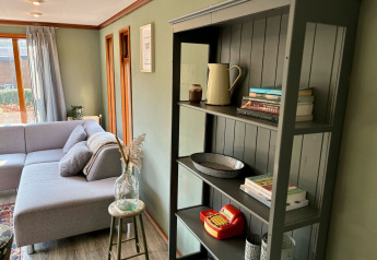 Hyggelig stue i Cozy Lodge ved Bungalowpark Het Verscholen Dorp med grå sofa og reol med bøger.
