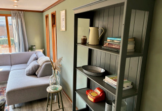 Hyggelig stue i Cozy Lodge ved Bungalowpark Het Verscholen Dorp med grå sofa og reol med bøger.