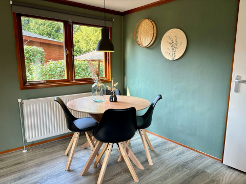 Eethoek met ronde tafel, vier zwarte stoelen en groene muur bij Cozy Lodge, Het Verscholen Dorp in Nederland.