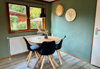Eethoek met ronde tafel, vier zwarte stoelen en groene muur bij Cozy Lodge, Het Verscholen Dorp in Nederland.