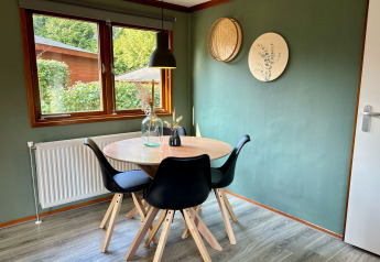 Comedor con mesa redonda, cuatro sillas negras y pared verde en Cozy Lodge, Het Verscholen Dorp, Países Bajos.