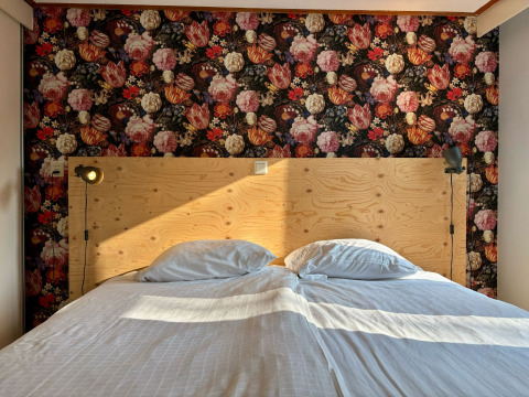 Slaapkamer in Cozy Lodge van Bungalowpark Het Verscholen Dorp met bloemenbehang en houten hoofdbord.
