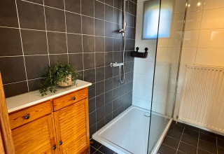 Badkamer met douche, zwarte tegels en houten kast bij Cozy Lodge in Bungalowpark Het Verscholen Dorp, Nederland.