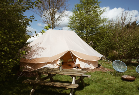Een Bell Tent Emperor-safaritent opgezet tussen bomen, met een picknicktafel en tuinstoelen ervoor.