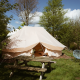 En Bell Tent Emperor-safari telt omgivet af grønne træer med et picnicbord og udendørs stole foran.