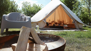 Billede af et Bell Tent 500 safari-telt med åbning, lejrbål og stol i en grøn, solrig natur.