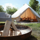 Billede af et Bell Tent 500 safari-telt med åbning, lejrbål og stol i en grøn, solrig natur.