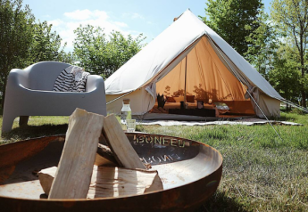 Foto eines Bell Tent 500 Safari-Zeltes mit offener Tür, Feuerschale und Sitzgelegenheit im Grünen.